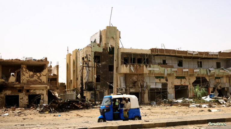 People pass by damaged cars and buildings at the central market in Khartoum North